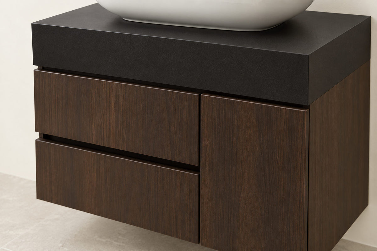 A modern floating bathroom vanity with a dark wood grain finish, featuring two drawers on the left and one larger cabinet door on the right, topped with a matte black slab countertop and a white vessel sink.