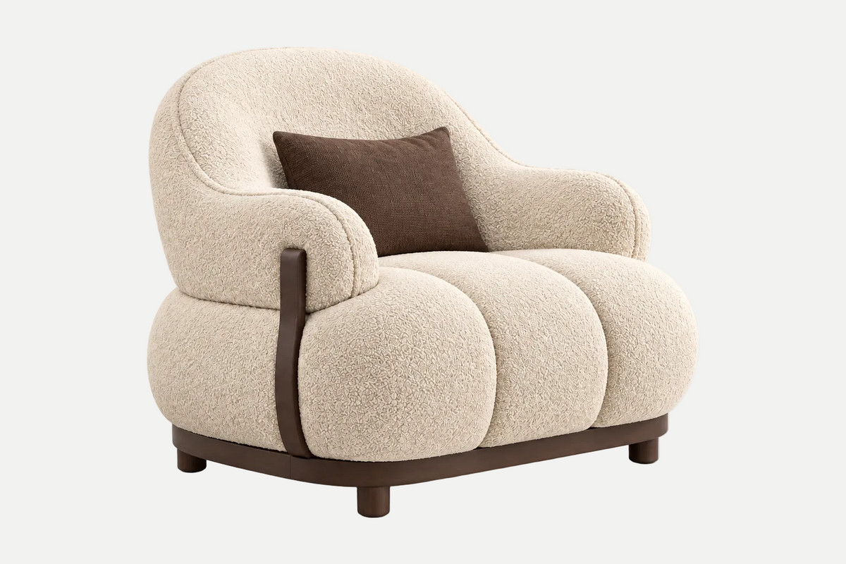 A modern curved armchair upholstered in textured cream bouclé fabric with dark brown leather trim and legs, featuring a matching brown accent pillow, set against a clean light gray background.