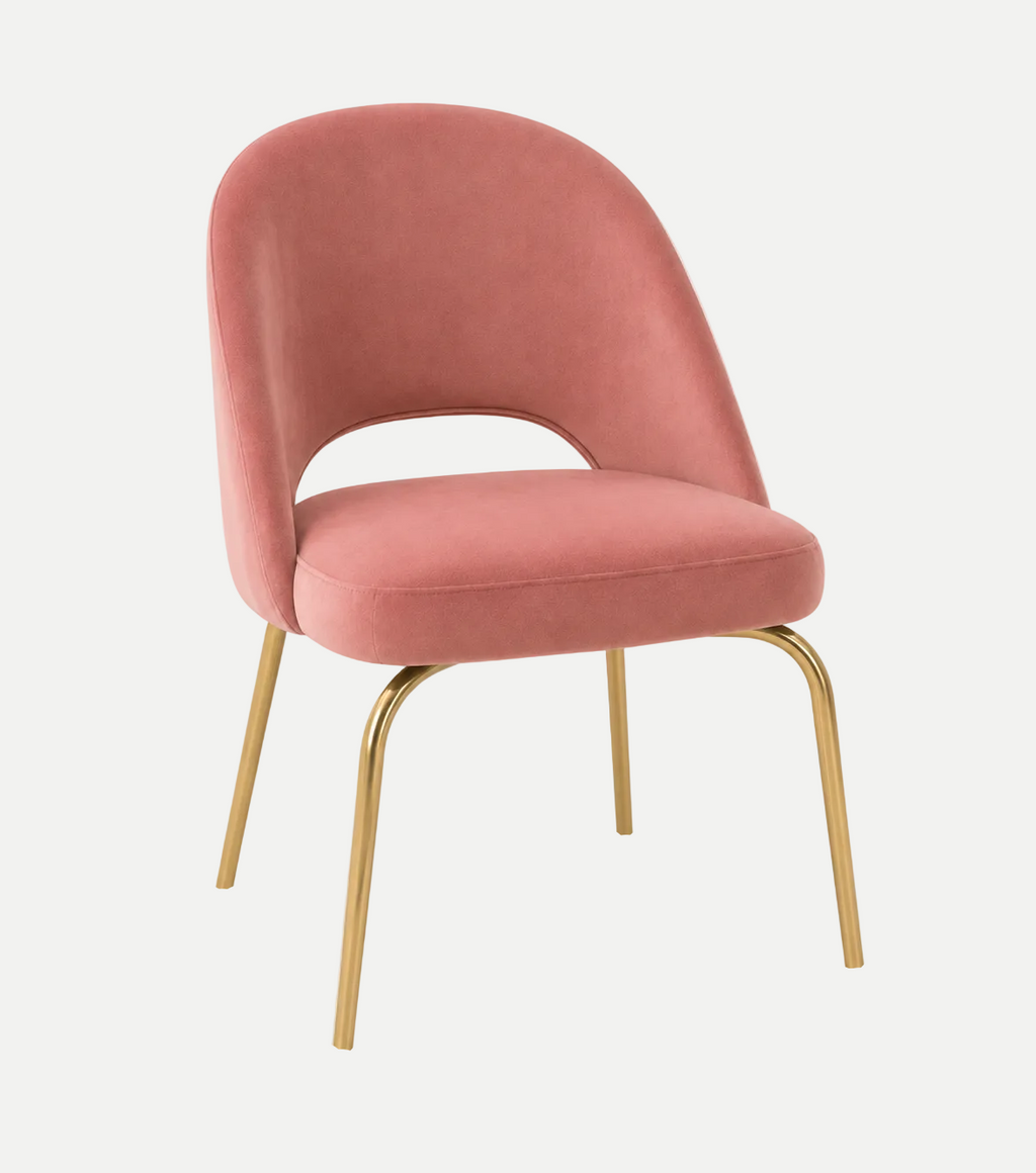 A modern accent chair with a pink velvet upholstered seat and curved backrest, supported by slim gold-finished metal legs, shown on a solid white background.
