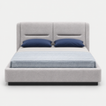 A modern platform bed with a light gray upholstered frame and tall segmented headboard, styled with two navy blue pillows and a textured blue-gray striped duvet, shown against a plain light gray background.