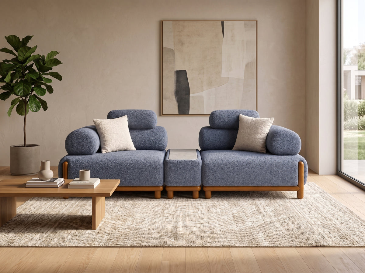 A modern two-seater sofa in textured blue fabric with light wood legs, styled in a minimalist living room with a matching area rug, wooden coffee table, and neutral wall art.