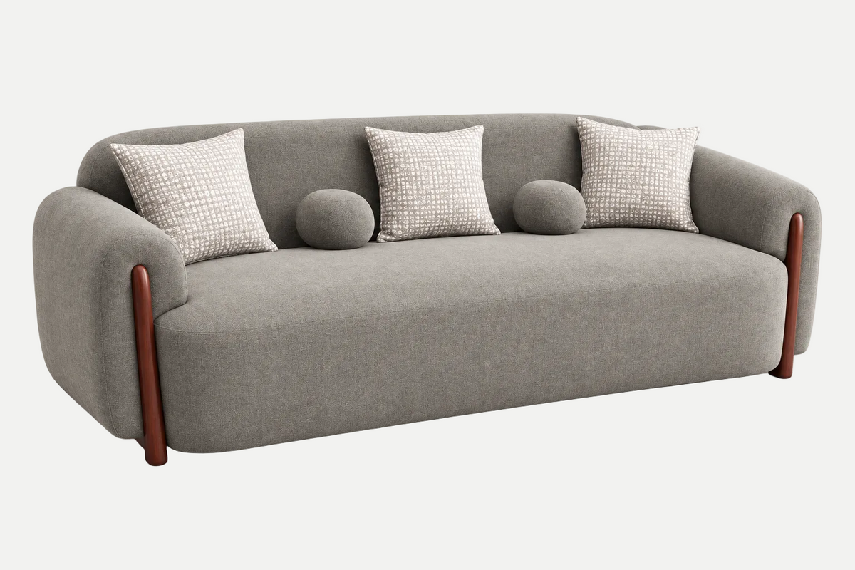 A modern gray upholstered sofa with rounded arms, four textured throw pillows, two round bolsters, and dark brown wooden legs, shown on a clean light gray background.