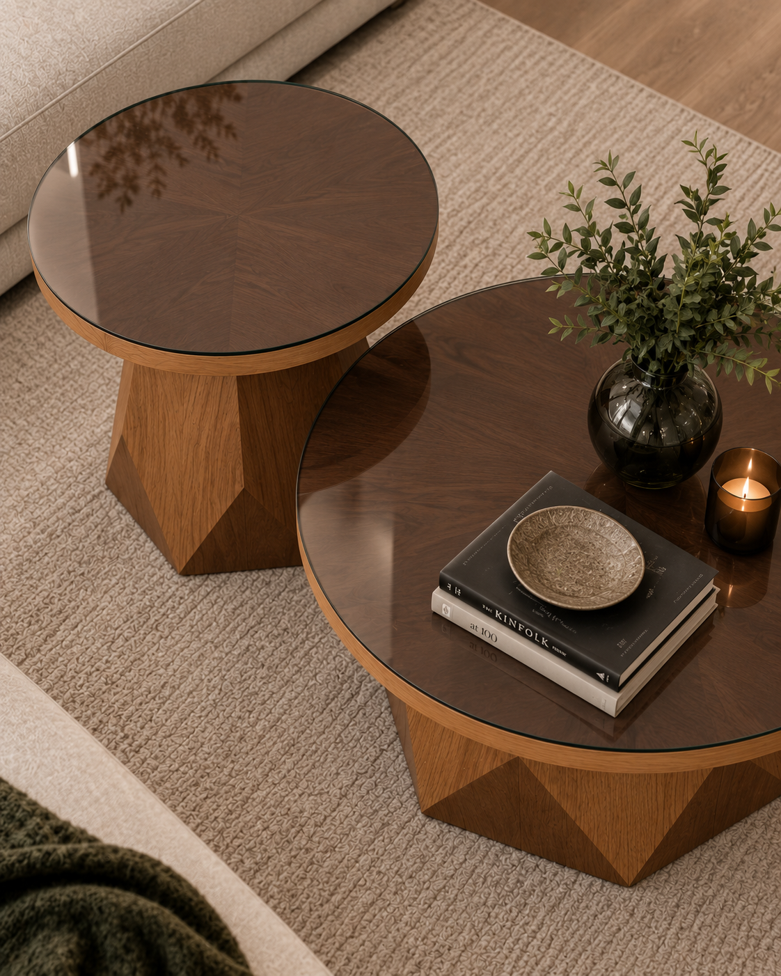 Two round nesting coffee tables with geometric wooden bases and dark wood tops, styled in a cozy living room setting with a rug, books, a bowl, and a plant.