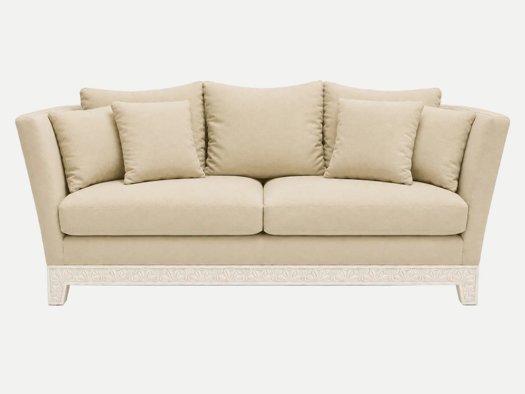A beige upholstered italian couch with four matching back cushions and a carved white base, shown against a plain light gray studio background.