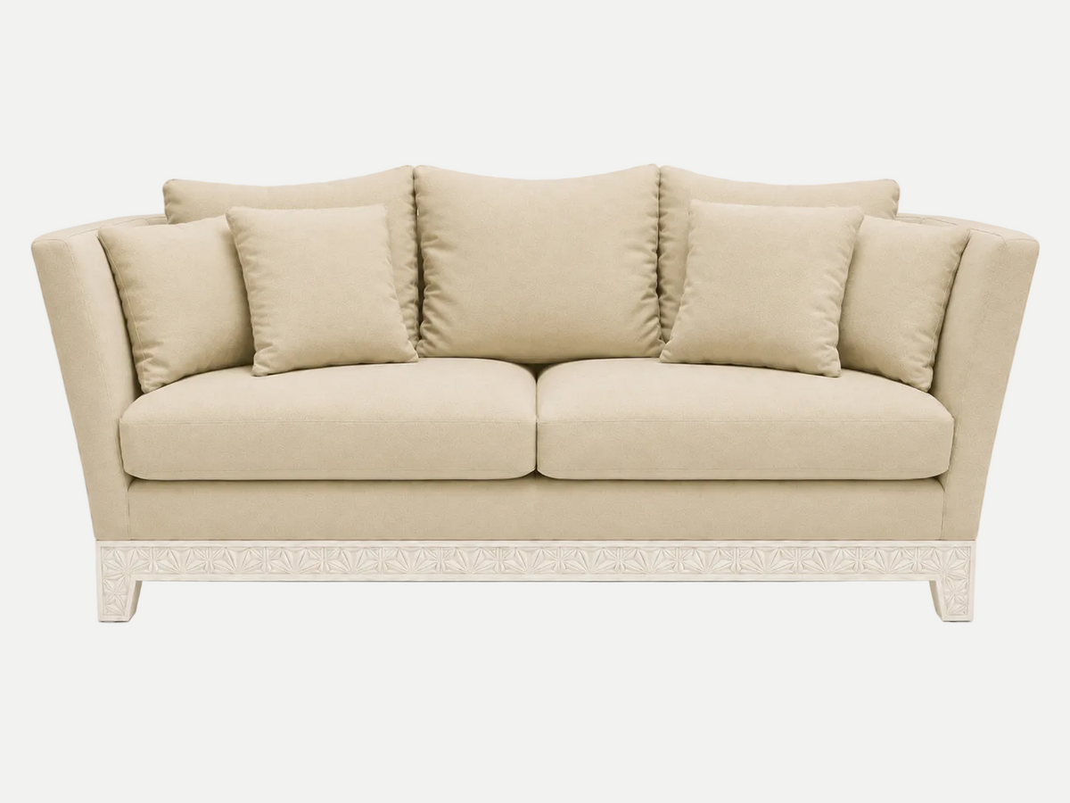 A beige upholstered italian couch with four matching back cushions and a carved white base, shown against a plain light gray studio background.