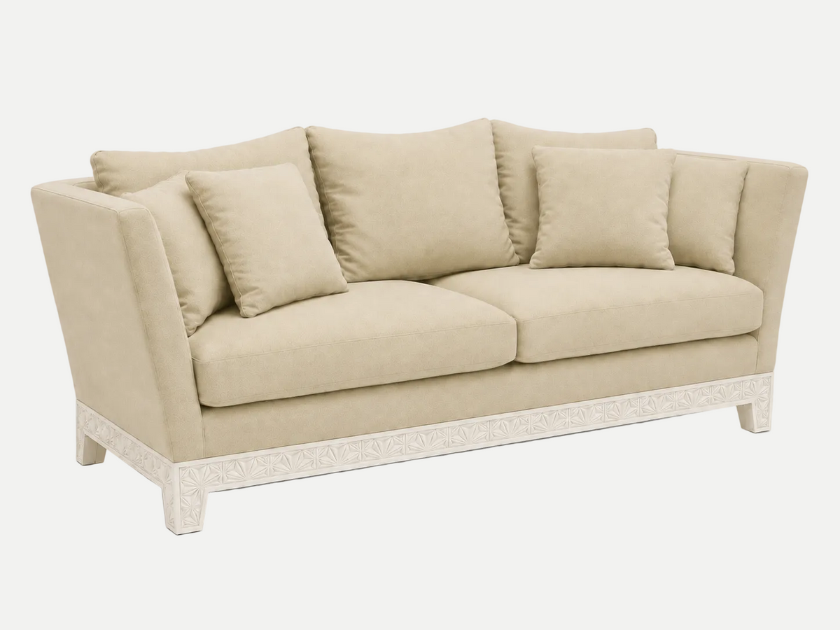A upholstered Italian Sofa in a warm beige fabric, featuring matching throw pillows and a carved white wooden base, shown against a plain white background.