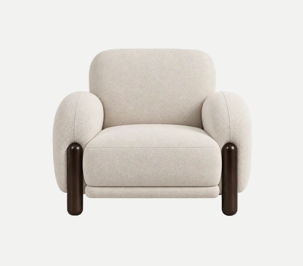 A modern upholstered armchair with rounded arms, a thick seat cushion, and beech wood, dark brown cylindrical legs, shown against a plain light gray studio background.