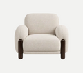 A modern upholstered armchair with rounded arms, a thick seat cushion, and beech wood, dark brown cylindrical legs, shown against a plain light gray studio background.