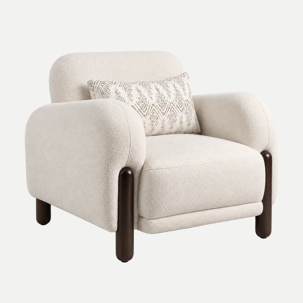 A modern upholstered accent chair in a textured cream bouclé fabric, featuring dark brown wooden legs and a matching cream patterned accent pillow, shown against a plain light gray background.