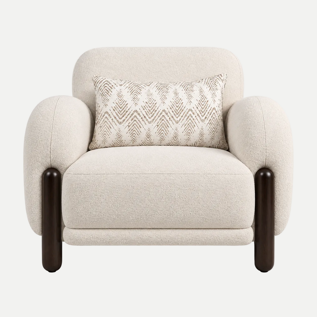 A modern upholstered accent chair in a textured cream bouclé fabric, featuring dark brown wooden legs and a matching cream throw pillow with a beige geometric pattern, set against a plain light gray background.