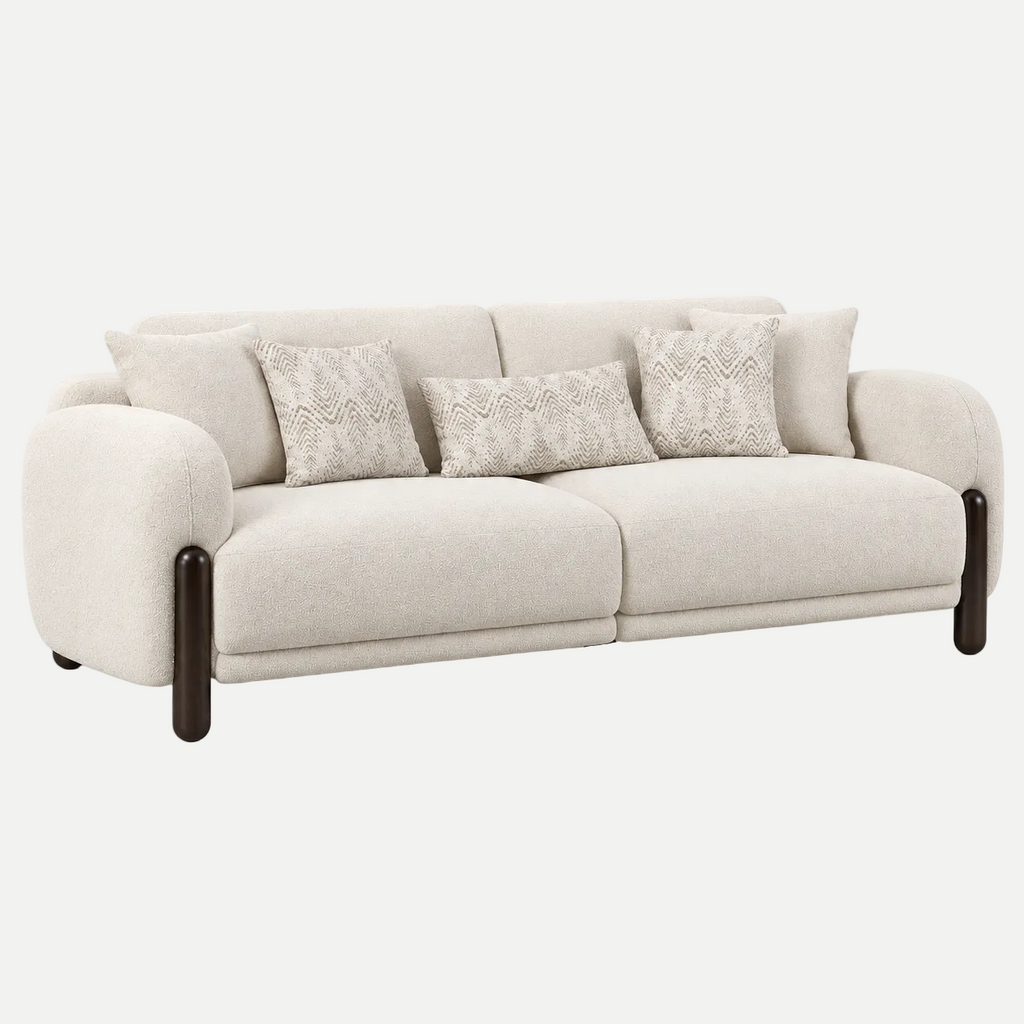 A modern three-seater sofa in a light beige textured fabric, featuring dark brown wooden legs and three decorative throw pillows, shown against a plain light gray background.