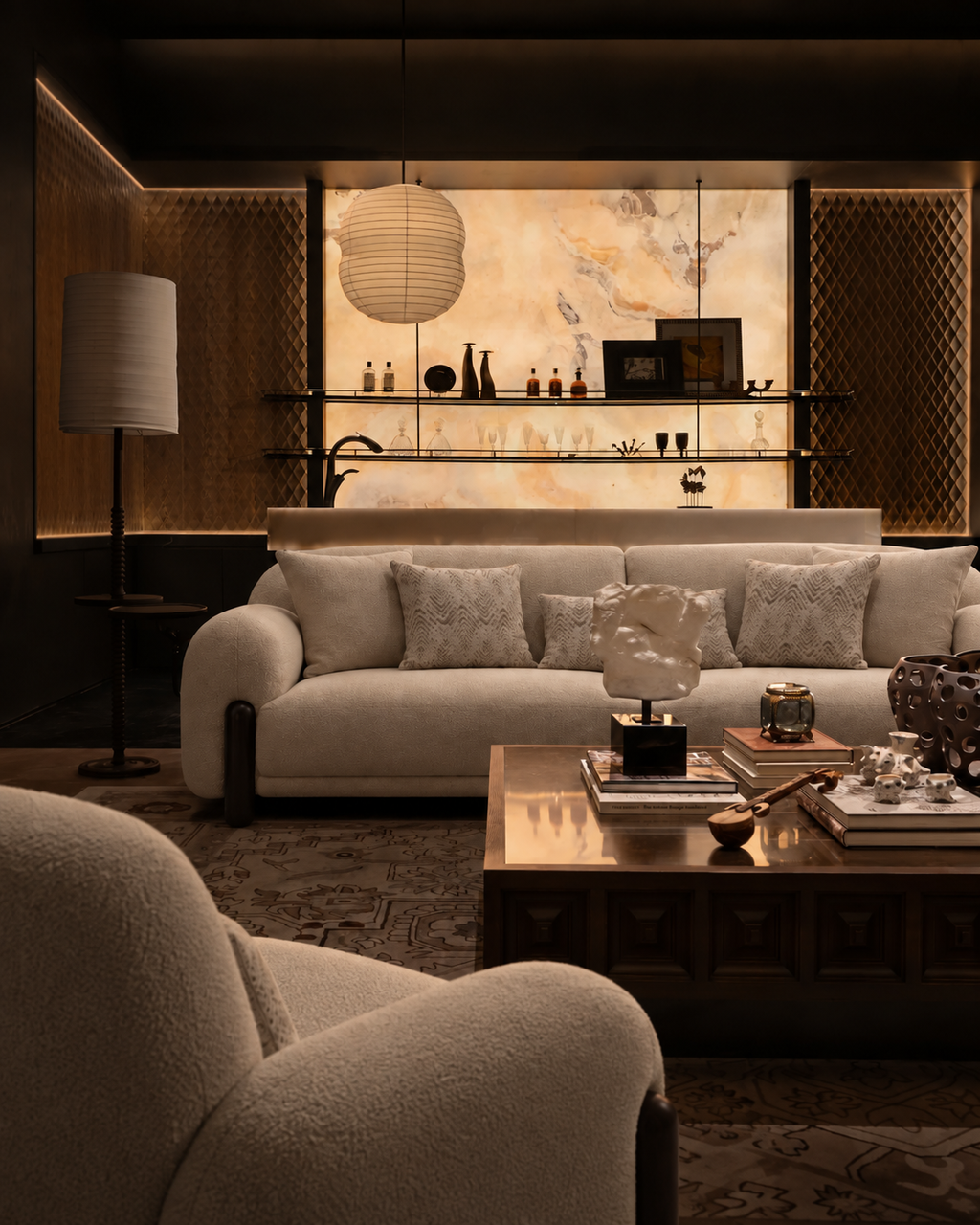 A luxury modern living room featuring a cream-colored sofa with textured throw pillows, a dark wood coffee table, and a warm, ambient background with a marble wall and decorative shelves.
