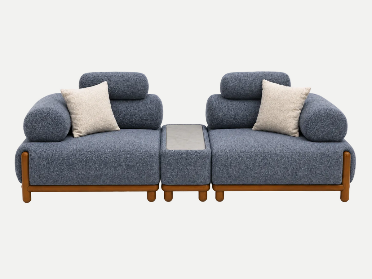 A modern modular sofa set with two blue-gray upholstered seat cushions, round backrests, light beige throw pillows, and a matching central ottoman with a gray top, all supported by a light wood frame, shown on a white background.