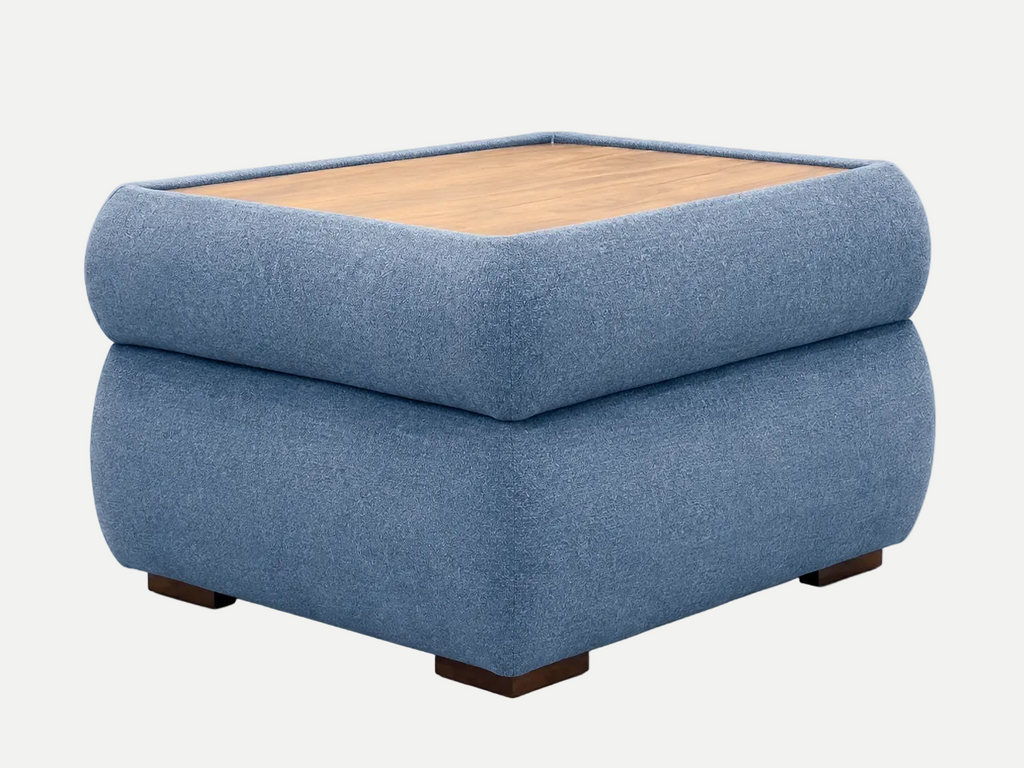 A square ottoman table upholstered in textured blue fabric, featuring a light wood top surface and dark wooden feet, shown against a plain off-white background.