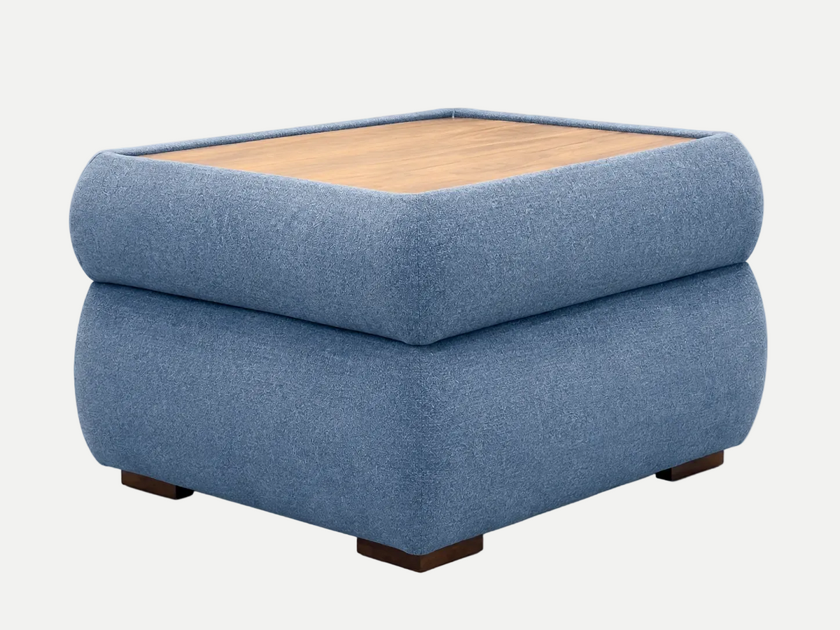 A square ottoman table upholstered in textured blue fabric, featuring a light wood top surface and dark wooden feet, shown against a plain off-white background.