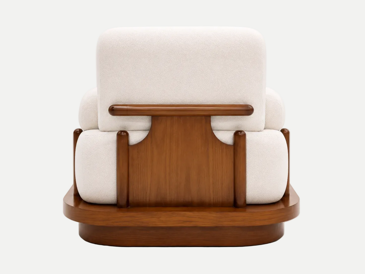 A mid-century modern armchair featuring cream-colored fabric cushions and a polished medium-brown wooden frame and base, shown from the back against a light gray studio background.