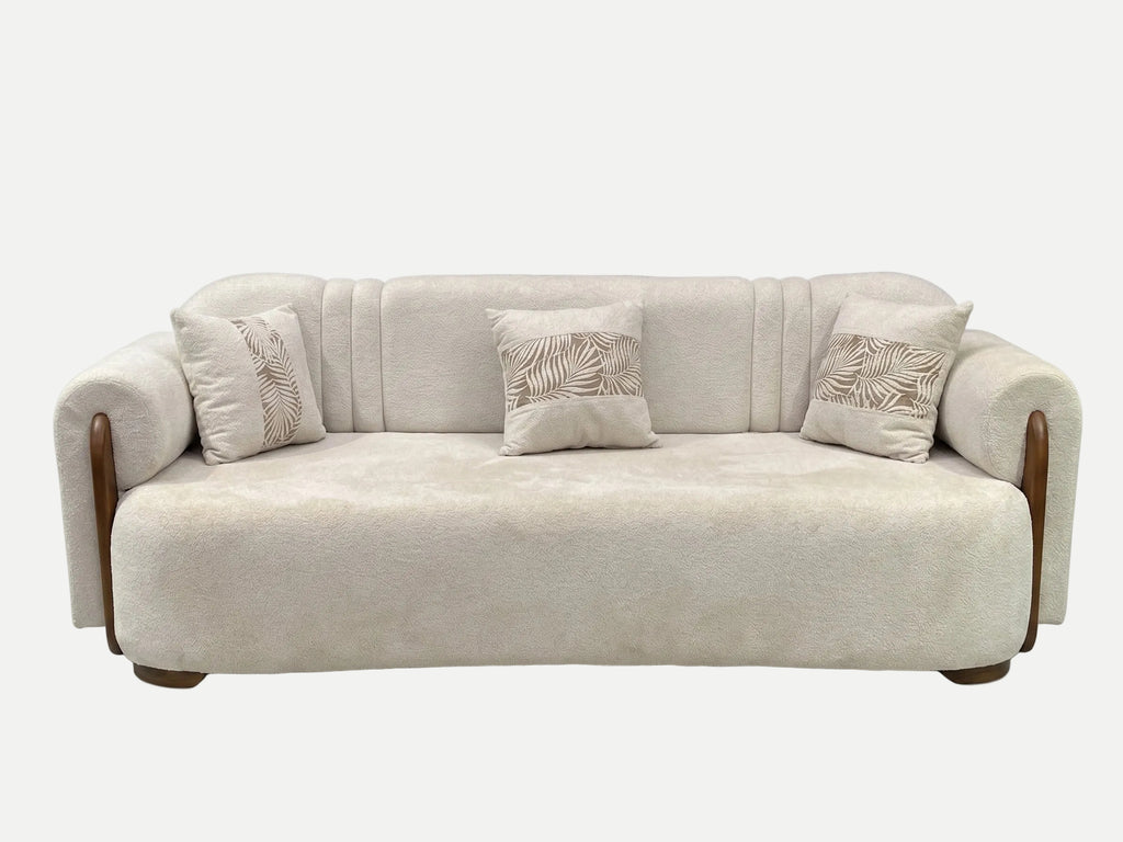A modern beige upholstered sofa with curved wooden arms and three matching decorative throw pillows featuring a leaf pattern, shown against a plain white background.