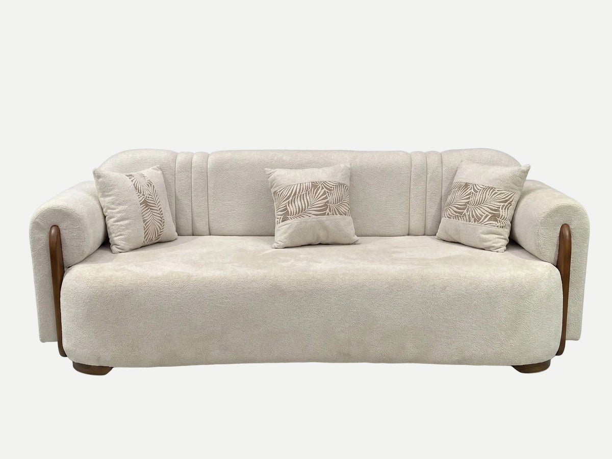 A modern beige upholstered sofa with curved wooden arms and three matching decorative throw pillows featuring a leaf pattern, shown against a plain white background.