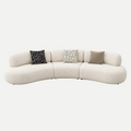 A curved modular upholstered sofa in a warm off-white fabric, styled with three decorative throw pillows (one black and white geometric pattern, one white and black geometric pattern, and one solid taupe) against a seamless light gray background.