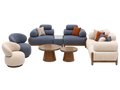 A mid-century modern furniture set featuring a blue modular sofa, a cream curved armchair, a matching cream sofa, two wooden coffee tables, and accent pillows, displayed on a light gray background.