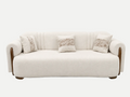 A cream-colored upholstered sofa with curved wooden arms and legs, featuring three decorative throw pillows with a beige palm leaf pattern, set against a plain white background.