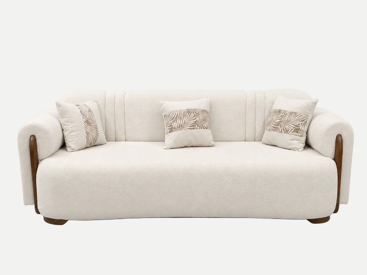 A cream-colored upholstered sofa with curved wooden arms and legs, featuring three decorative throw pillows with a beige palm leaf pattern, set against a plain white background.