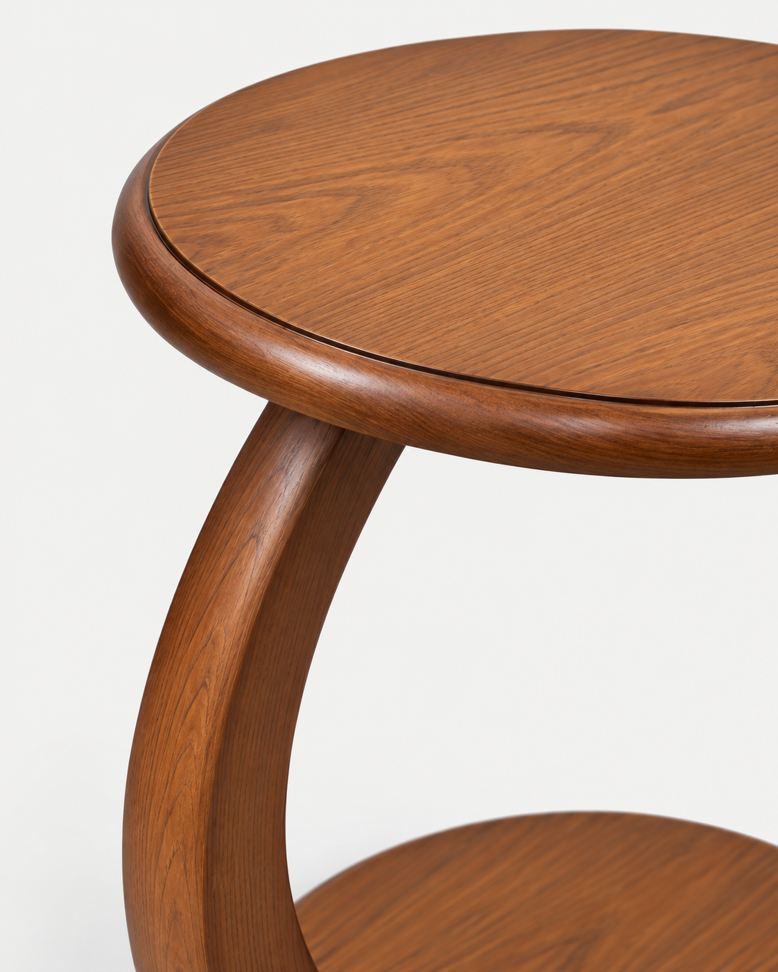 Close-up of a round wooden side table with a warm medium-brown finish, showing the tabletop edge, curved support leg, and part of a lower shelf against a plain white background.