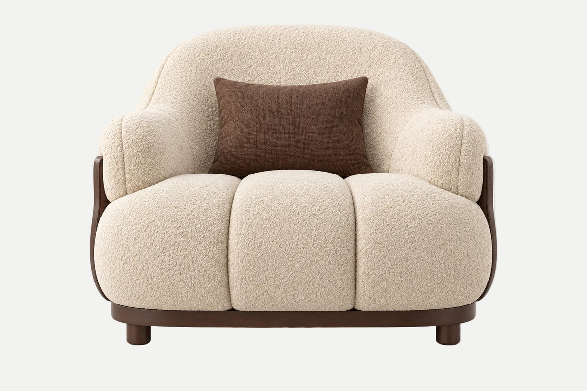 A modern low-profile armchair with textured cream bouclé upholstery, dark brown wooden arms and base, and a single dark brown accent pillow, shown against a plain light gray background.