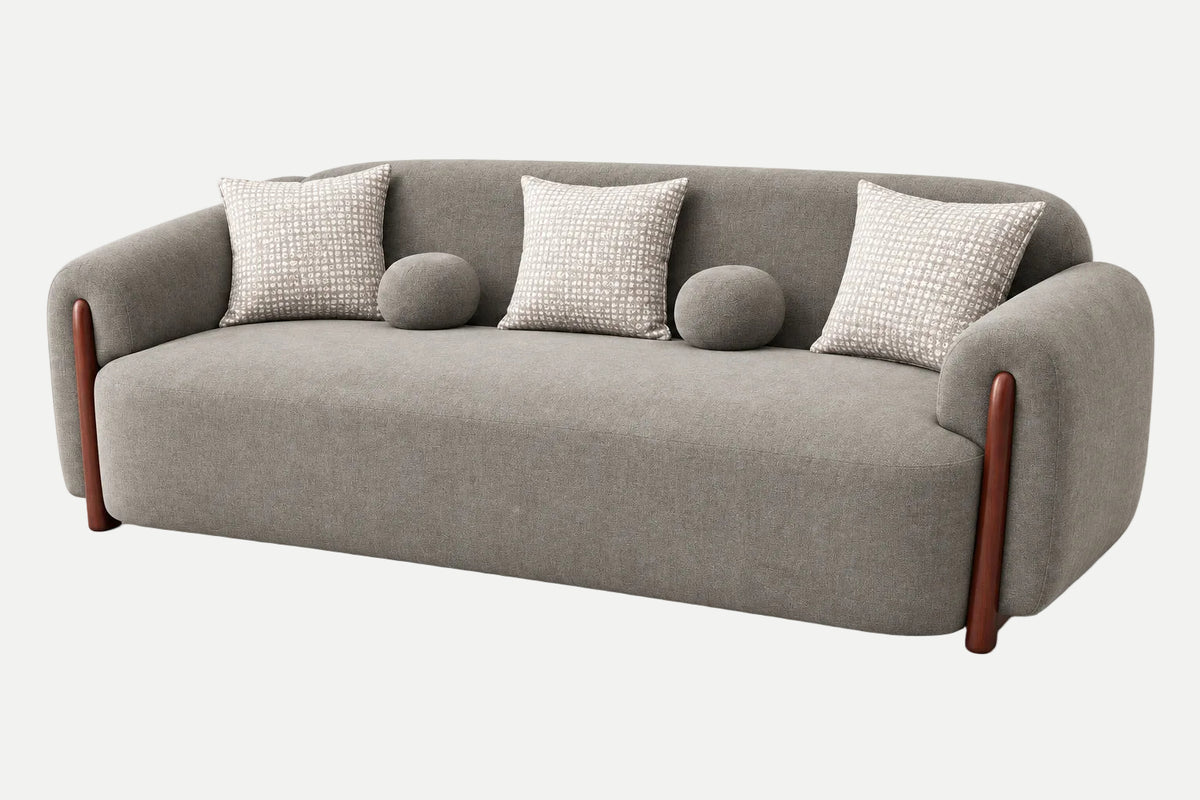 A modern gray upholstered sofa with rounded arms, four textured throw pillows, two round bolsters, and dark brown wooden legs, shown on a clean light gray background.