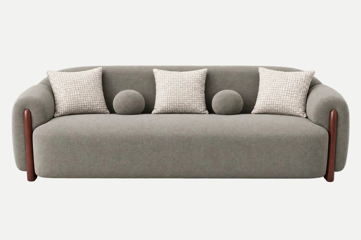 A modern gray upholstered sofa with rounded arms, dark wood legs, four textured light beige throw pillows, and two round matching gray pillows, shown on a clean white background.