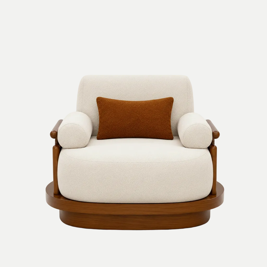 A lounge chair with a thick cream upholstered seat and back, cylindrical armrests, a dark wood base and arm supports, and a small rectangular rust-brown accent pillow, shown against a plain light beige studio background.